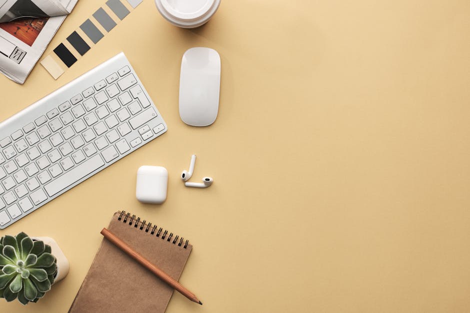 A minimalist workspace flat lay with keyboard, mouse, notebook, and succulent on a beige background.